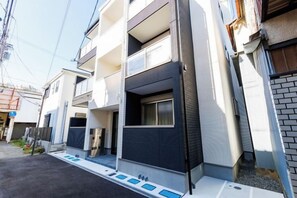 A modern multi-story residential building with balconies, a garage, and a small front yard.