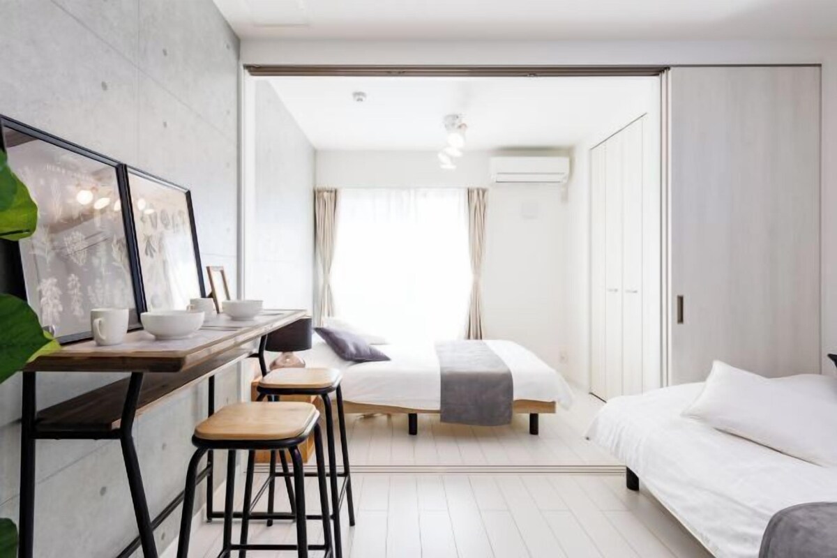A modern bedroom with a bed, a desk with stools, and a large window.