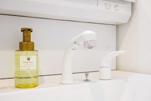 A bathroom with a white sink, a gold pump bottle of foam soap, and a white faucet.
