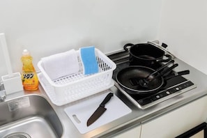 A kitchen with a sink, a cutting board, a knife, a frying pan, and a bottle of dish soap.
