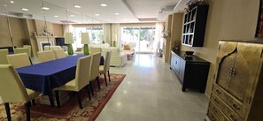 A spacious dining area with a long table, chairs, and a patterned rug.