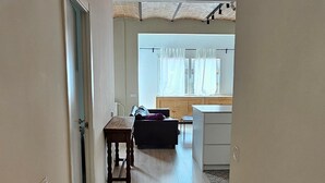 Een gang met houten vloer die leidt naar een kamer met raam, tafel en stoel.