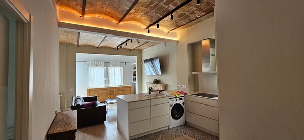 A compact kitchen with a washing machine, a sink, and a window with curtains.