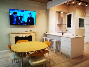 Une cuisine moderne dotée d’un îlot central, d’un coin repas avec une table et des chaises, et d’un téléviseur à écran plat fixé au mur.