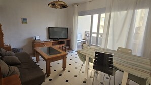 A living room with a sofa, a TV, a wooden coffee table, and a dining table with chairs. - Holiday Home 'Centrico Piso En Marbella' with Private Terrace and Wi-Fi (Marbella)