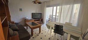 A living room with a sofa, a TV, a wooden coffee table, and a dining table with chairs.