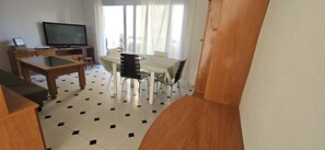 A living room with a TV, a dining table with chairs, a sofa, and a staircase.