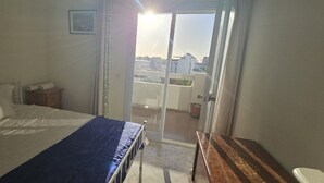 A bedroom with a bed, a wooden nightstand, a window with a view of buildings, and a door leading to a balcony. - Holiday Home 'Centrico Piso En Marbella' with Private Terrace and Wi-Fi (Marbella)