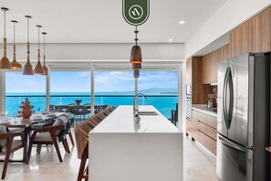 A modern kitchen with a large island, stainless steel appliances, and a view of the ocean.