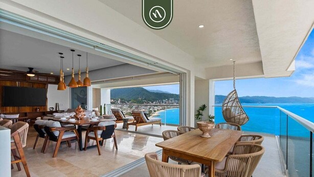 A spacious dining area with a wooden table and wicker chairs, overlooking a scenic coastal view. - Luxury 4 BR Condo Amazing Views - Beach - Pools (Puerto Vallarta)