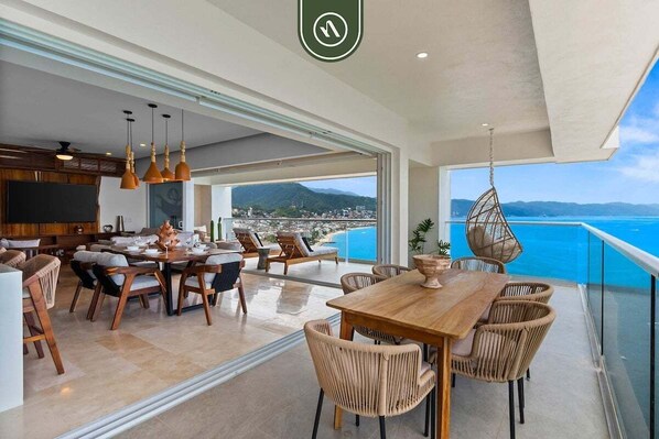 Un comedor amplio con una mesa de madera y sillas de mimbre, con vistas a un paisaje costero.