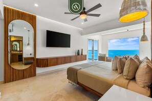 A modern bedroom with a bed, a TV, a ceiling fan, and a view of the ocean.