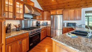 Una cocina con armarios de madera, electrodomésticos de acero inoxidable, encimeras de granito y techo de madera.