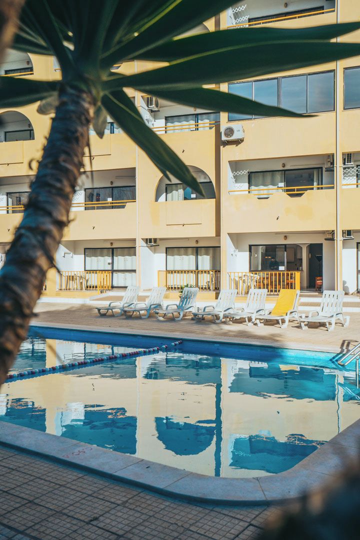Ein Schwimmbecken mit Liegestühlen und ein Gebäude mit Balkonen im Hintergrund.