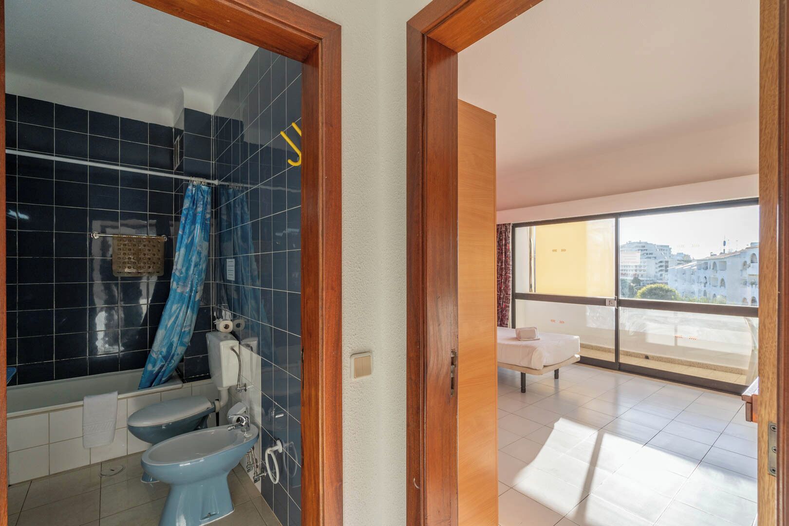 Un baño con inodoro, bidé y ducha, y un balcón con vistas a edificios.