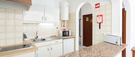 A modern kitchen with white cabinets, granite countertops, a built-in microwave, and a water heater.
