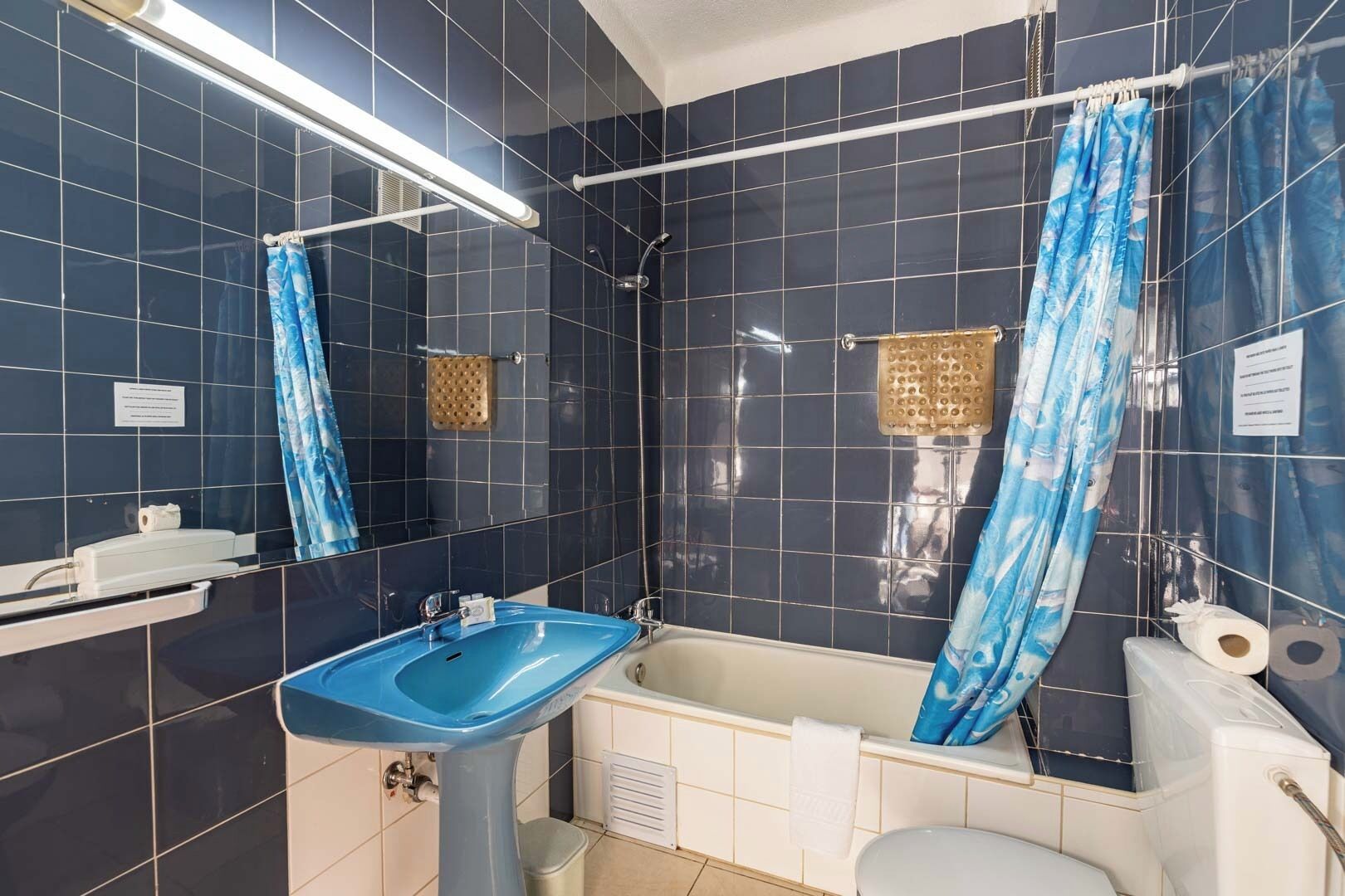A bathroom with dark blue tiles, a blue sink, a bathtub, and a shower curtain.