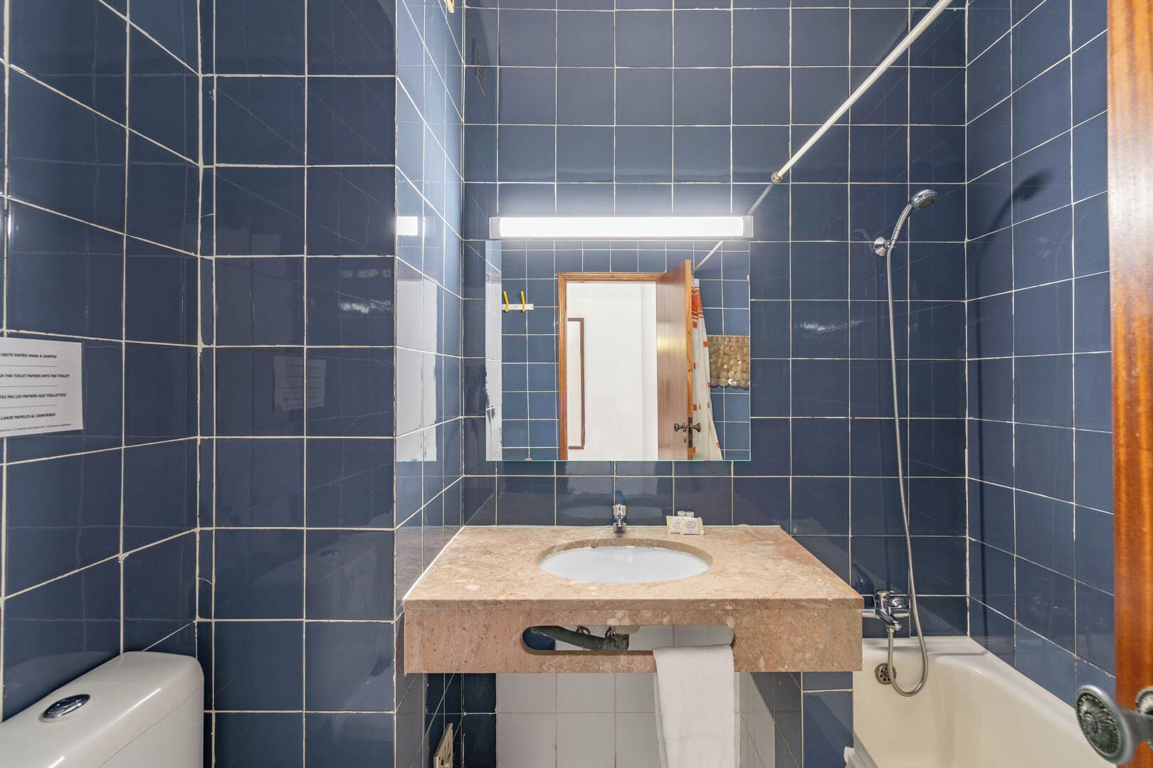 Une salle de bain avec des carreaux bleu foncé, un lavabo avec un miroir, un porte-serviettes et une douche.