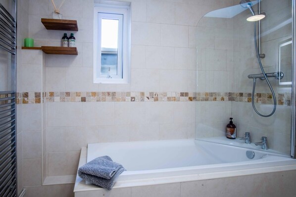 A modern bathroom with a bathtub, a shower, and a window. - The Nook North Beach - 1 Bedroom Apartment - Tenby (Tenby)