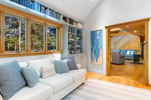 Un salon moderne avec un canapé blanc, des étagères, une grande fenêtre et un escalier menant à une autre pièce.