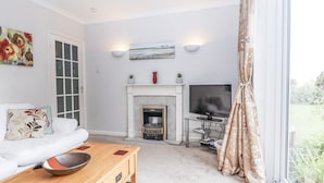 A living room with a white sofa, a wooden coffee table, a fireplace, a TV on a stand, and a window with curtains.