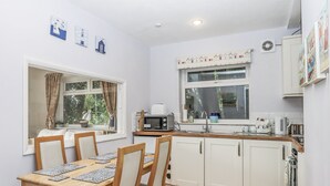 A compact kitchen with white cabinets, a wooden dining table with four chairs, a microwave, and a window with curtains.