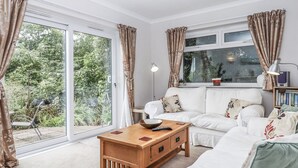 A living room with a white sofa, a wooden coffee table, and a large window with curtains.