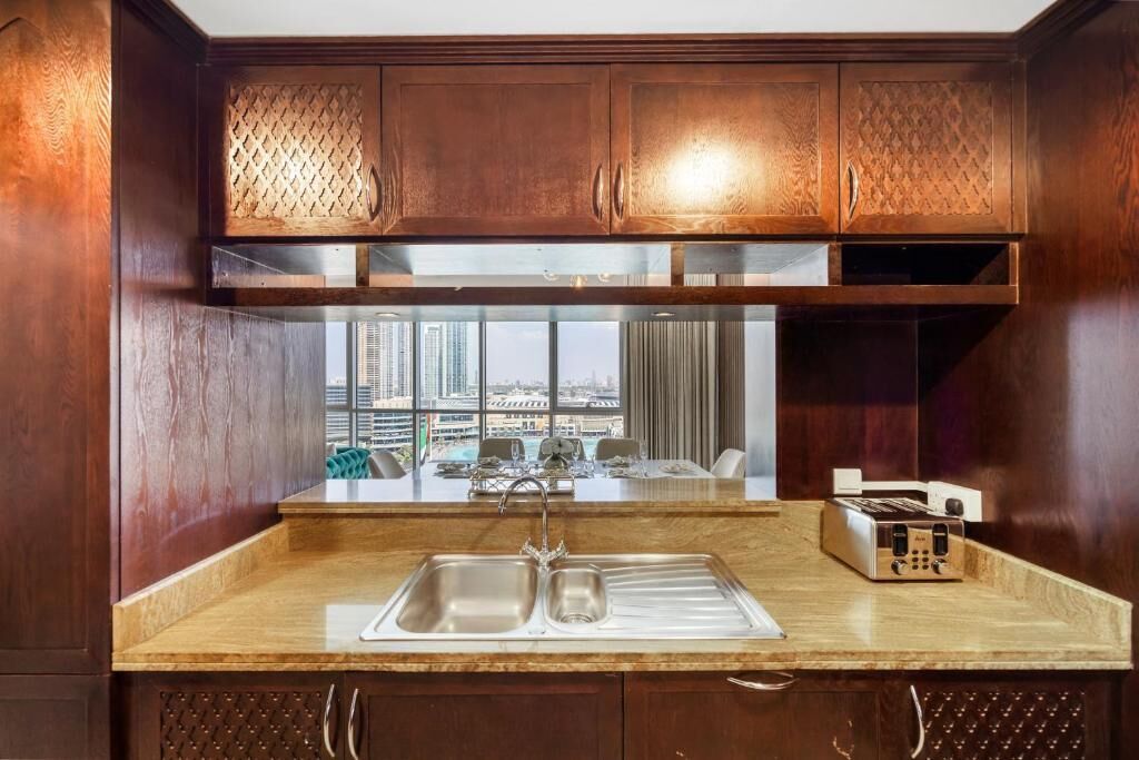 A modern kitchen with a stainless steel sink, wooden cabinets, and a view of the city through large windows.