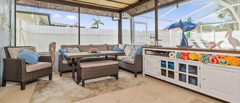 A covered outdoor seating area with wicker furniture, a table, and a cabinet with decorative items.