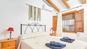 A bedroom with a bed, two bedside tables, a red lamp, a window with wooden shutters, and an air conditioning unit.