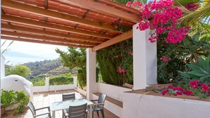 An outdoor patio with a pergola, a table with chairs, and potted plants.