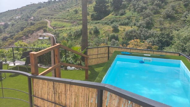 A pool with a view of a hilly landscape, bamboo fencing, and a wooden deck.