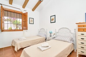 Une chambre avec deux lits, une fenêtre avec des rideaux, une table de chevet avec une lampe et une commode avec des tiroirs.