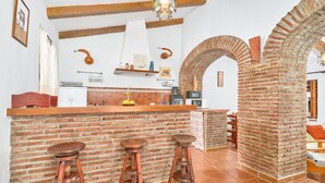 A kitchen with a brick island, stools, a hanging light fixture, and a brick archway.