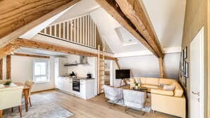 A spacious loft with a kitchen, dining area, and a cozy seating area under exposed wooden beams. - Ferienwohnung Alpen Zentral (Bludenz)