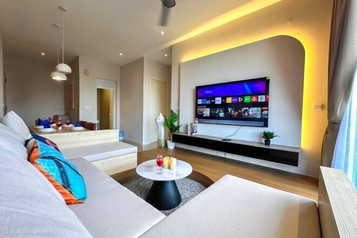 Una sala moderna con un televisor de pantalla plana montado en la pared, un sofá con cojines coloridos y una mesa de centro con una copa y velas.