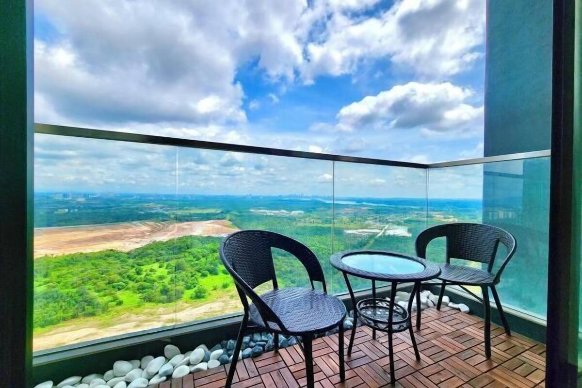 Un balcón con dos sillones de mimbre y una mesita, con vista a un paisaje verde bajo un cielo despejado.