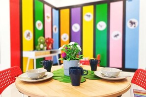 A round wooden table with four blue cups and saucers, a white pitcher, and a potted plant. The background features a colorful wall with vertical panels and circular icons. - D'Pristine Legoland by RR JBcity (Iskandar Puteri)