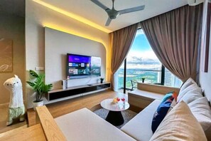Un salon moderne doté d’un téléviseur à écran plat, d’un ventilateur de plafond, d’un canapé, d’une table basse et d’une grande fenêtre avec des rideaux.