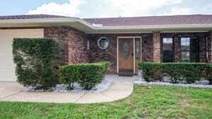 A two-story brick house with a front garage, a wooden front door, and a small front yard with trimmed bushes. - Cozy 4bed 2bth villa - daytona beach  (Deltona)