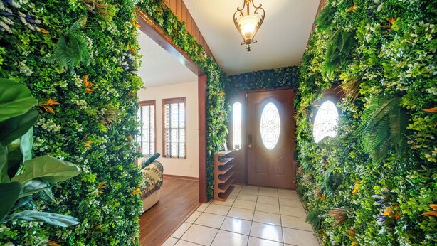 A hallway with a green wall covered in plants, a wooden door with a window, and a tiled floor. - Cozy 4bed 2bth villa - daytona beach  (Deltona)