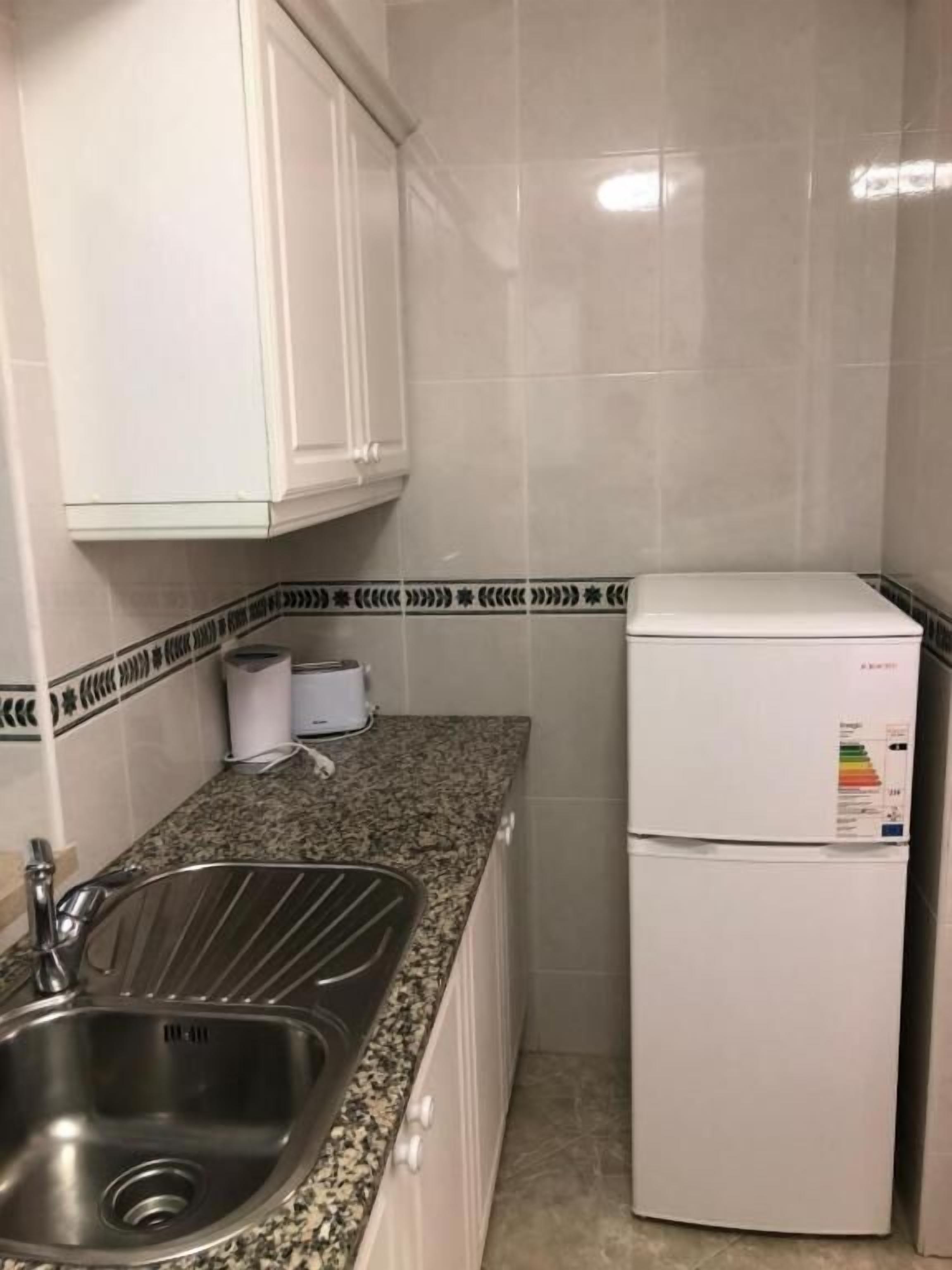 A small kitchen with a stainless steel sink, a white refrigerator, and a toaster on the countertop.