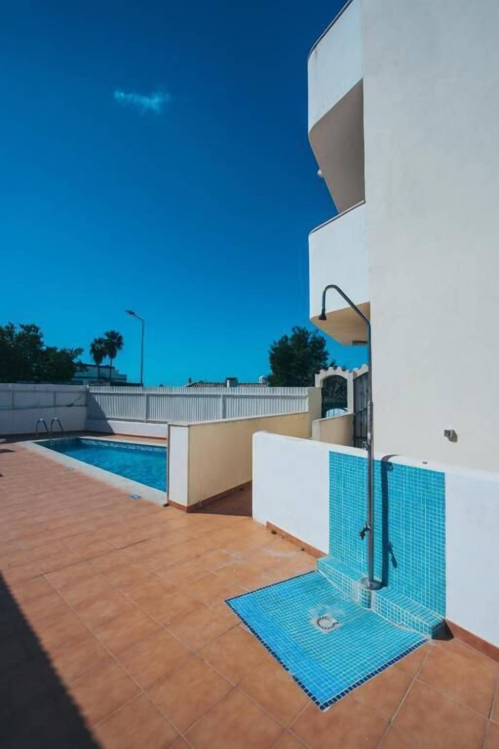 Zona de piscina amb solàrium enrajolat, escala de piscina i mur amb secció revestida de blau.