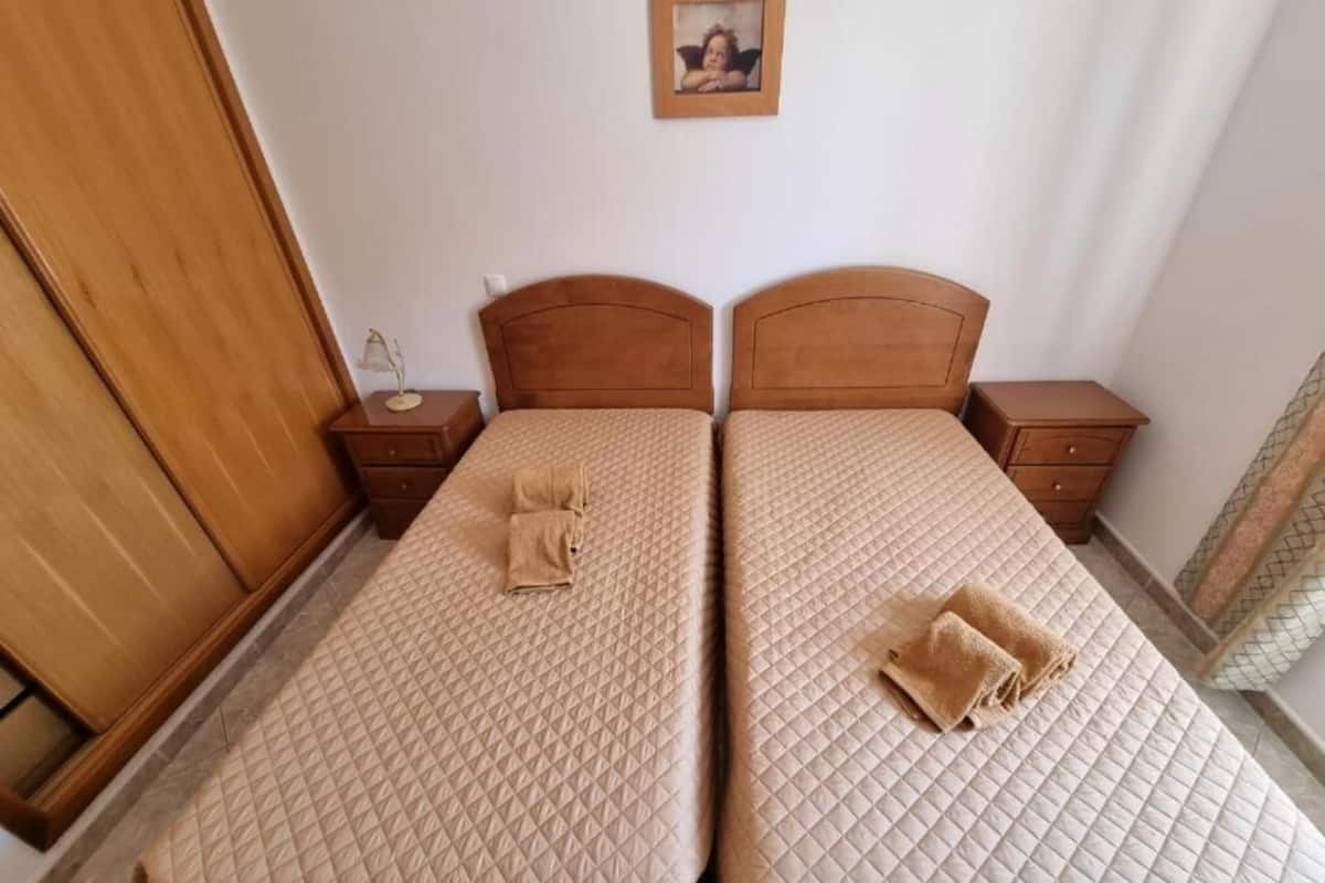 A room with two beds, each with a wooden headboard, a bedside table, and a lamp.