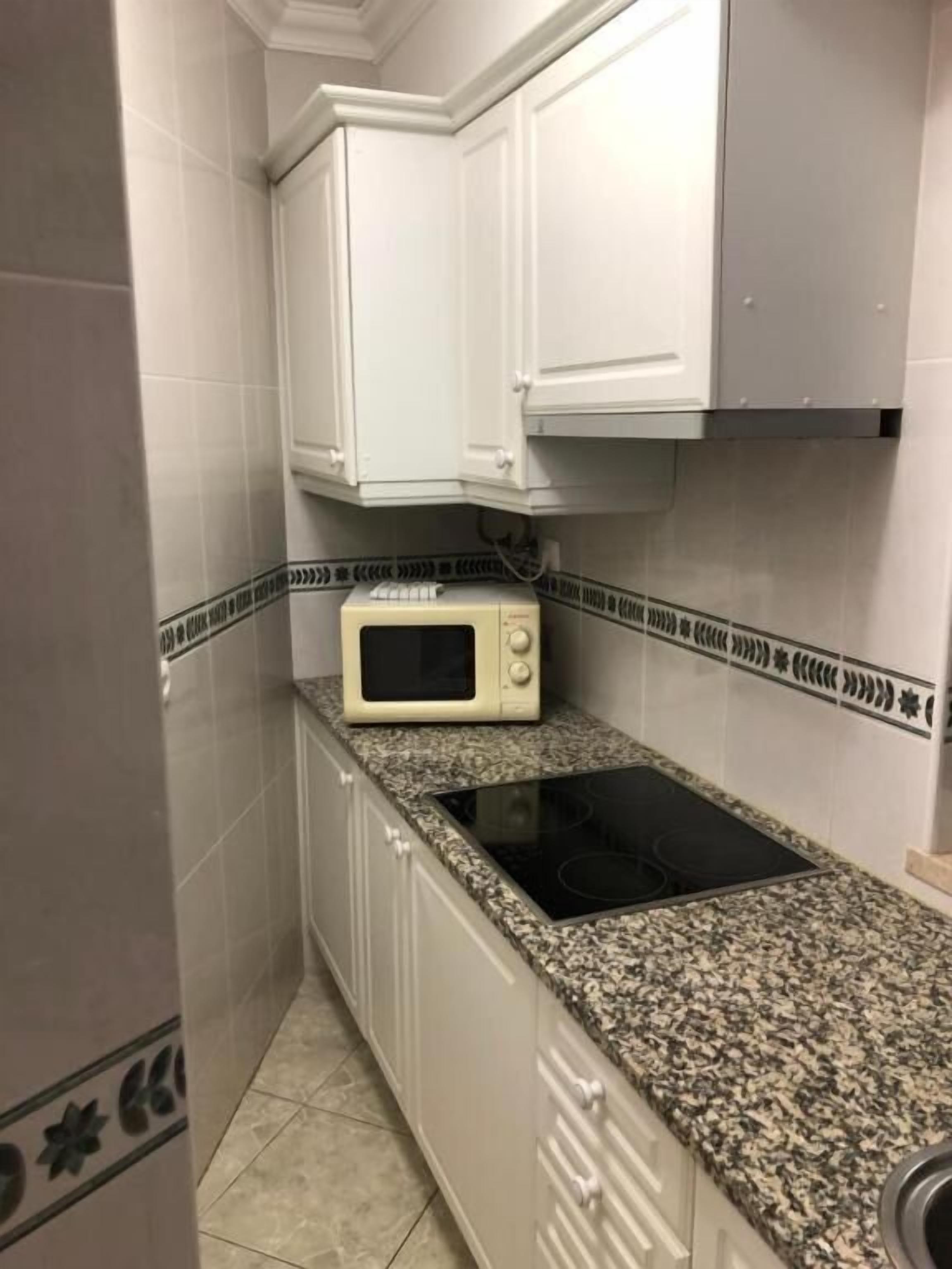 A small kitchen with white cabinets, a microwave, and a granite countertop.