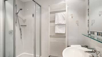 A modern bathroom with a glass-enclosed shower, a white bathtub, a glass-topped vanity, and a towel rack.