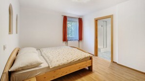 Une chambre à coucher avec un lit en bois, une fenêtre avec des rideaux rouges et une porte donnant sur une salle de bain.