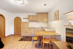 A modern kitchen with wooden cabinets, a dining table with chairs, and a built-in TV.