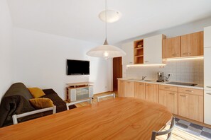 Une cuisine moderne avec des meubles en bois, une table à manger et un téléviseur fixé au mur.