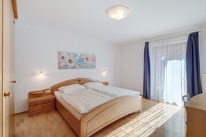 Une chambre à coucher avec un lit en bois, des tables de chevet, une lampe fixée au mur, une fenêtre avec des rideaux et un tableau représentant des motifs floraux.